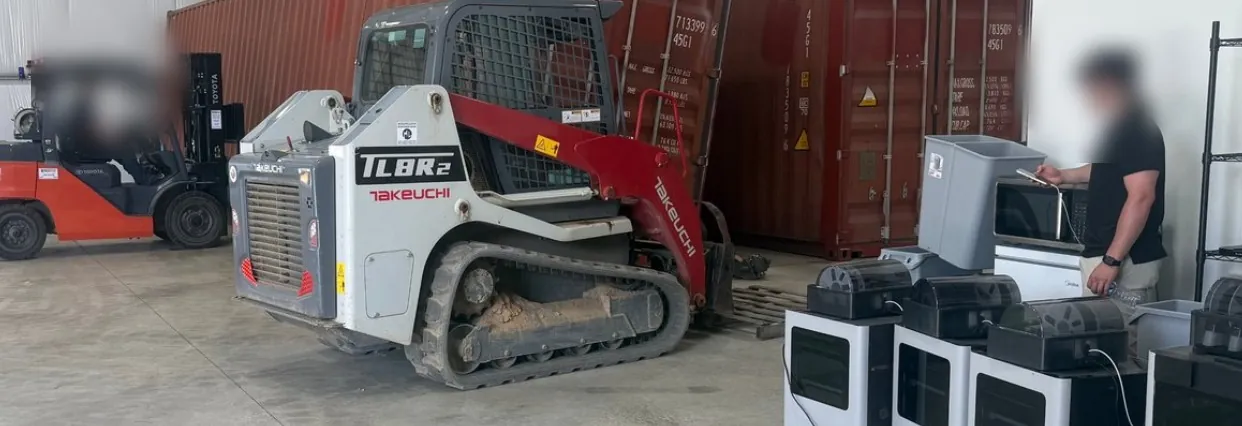 The Flat Rate Movers warehouse — red shipping containers with a Toyota forklift, a Takeuchi track loader and crew working alongside equipment lined up on the warehouse floor